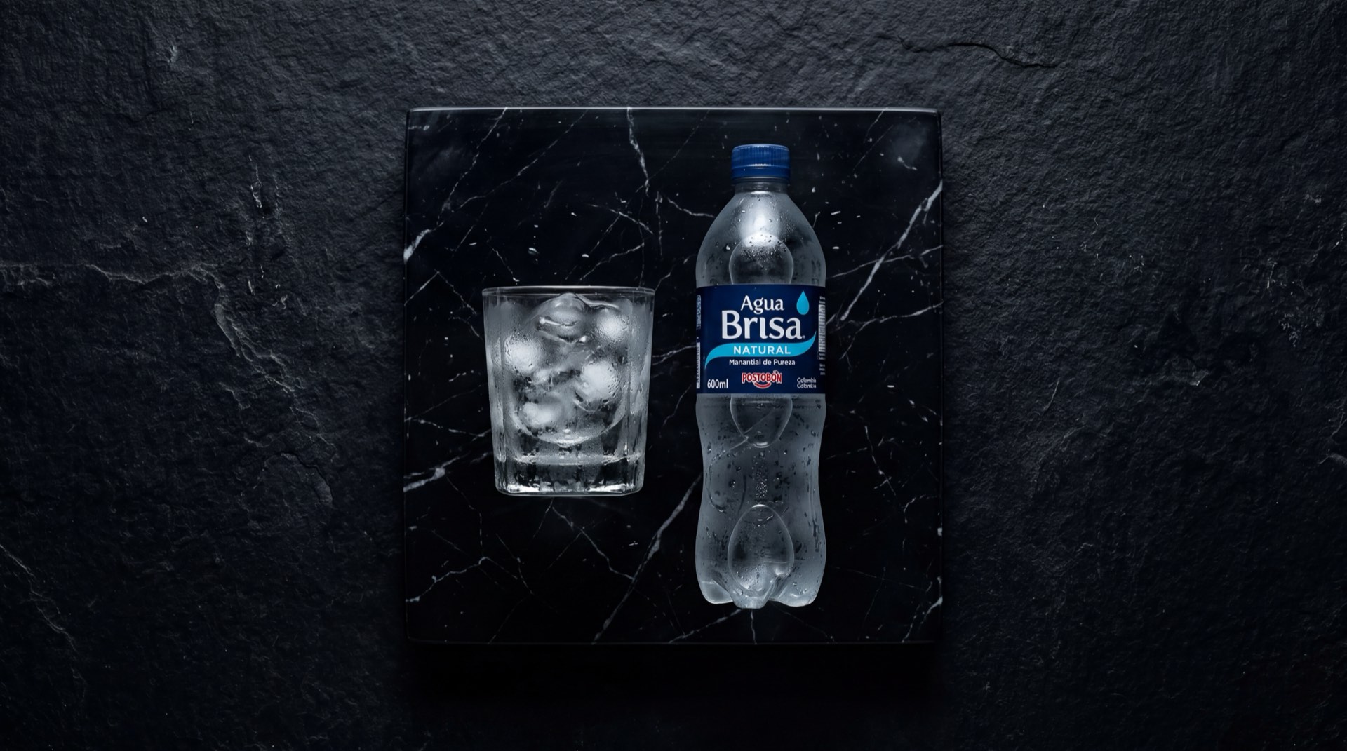 Botella de Agua Brisa de Postobon con etiqueta azul sobre mesa de marmol negro