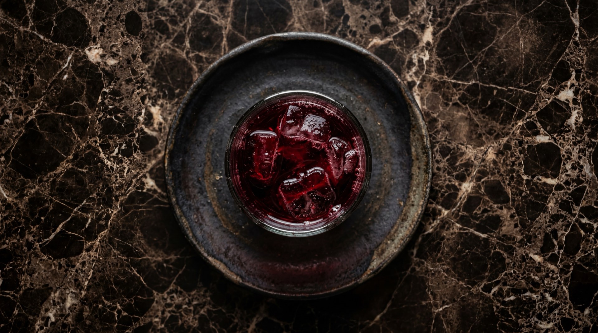 Agua de jamaica mexicana color rojo intenso en vaso de vidrio alto con hielo sobre mesa de marmol negro con vetas doradas