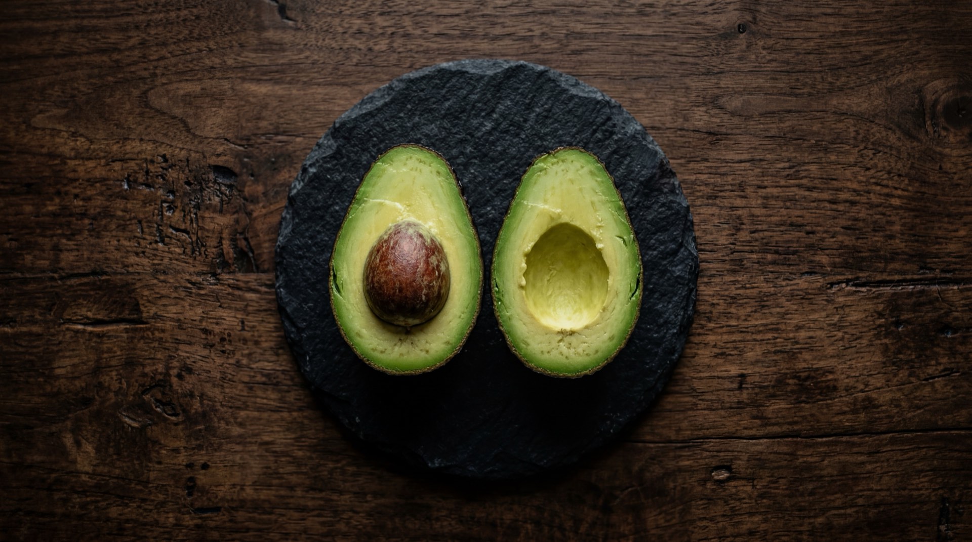 Aguacate colombiano maduro cortado por la mitad mostrando la pulpa verde cremosa en plato de ceramica negra mate sobre mesa de marmol negro con vetas doradas