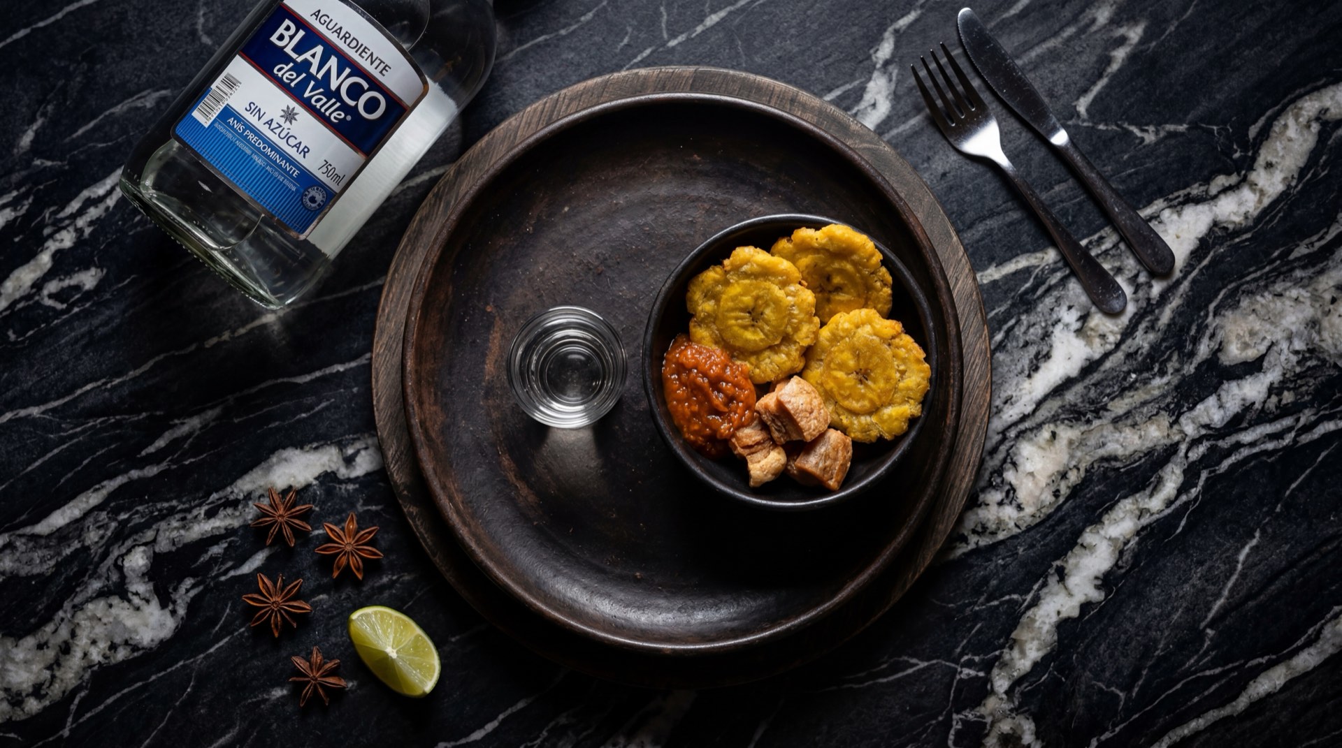 Botella de aguardiente Blanco del Valle con shot servido en vaso de vidrio transparente sobre mesa de nogal oscuro
