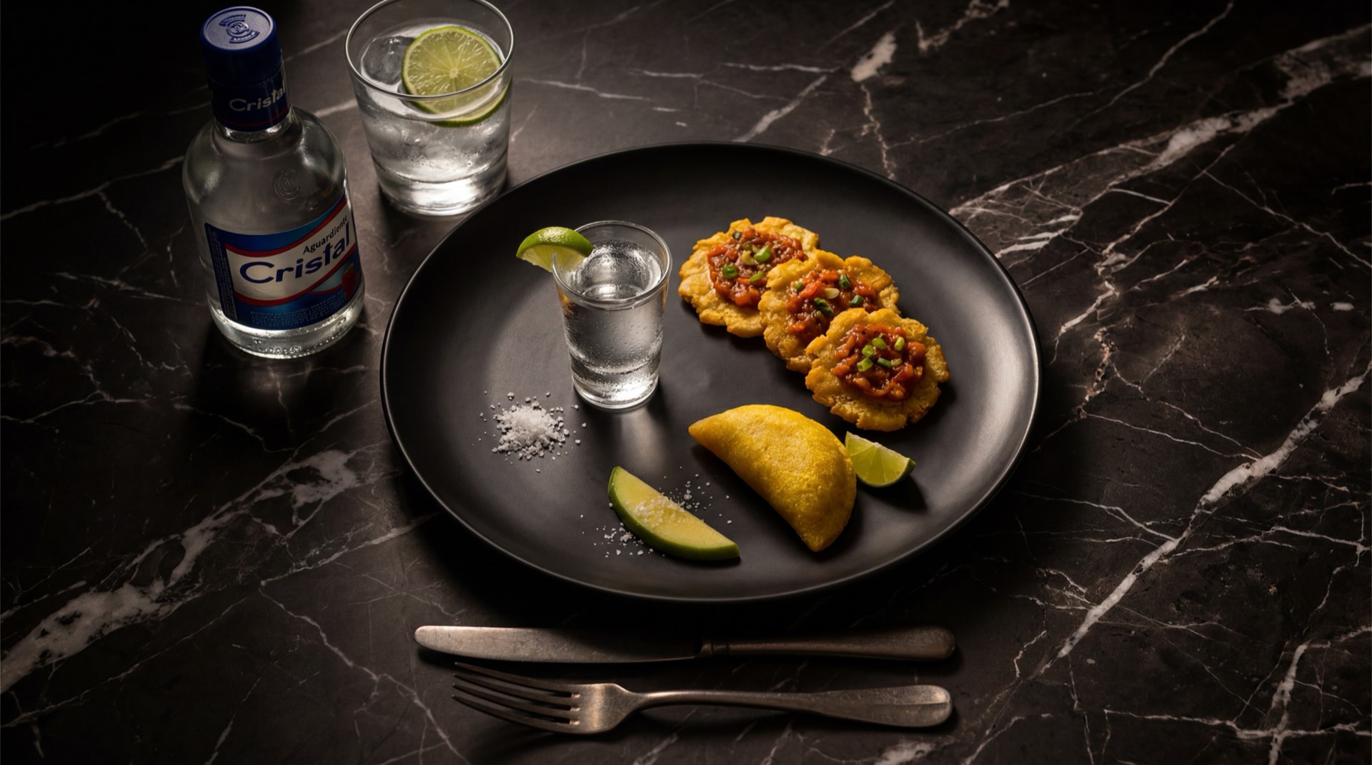 Botella de aguardiente Cristal antioqueno con shot servido en vaso de vidrio transparente sobre mesa de granito negro con destellos dorados