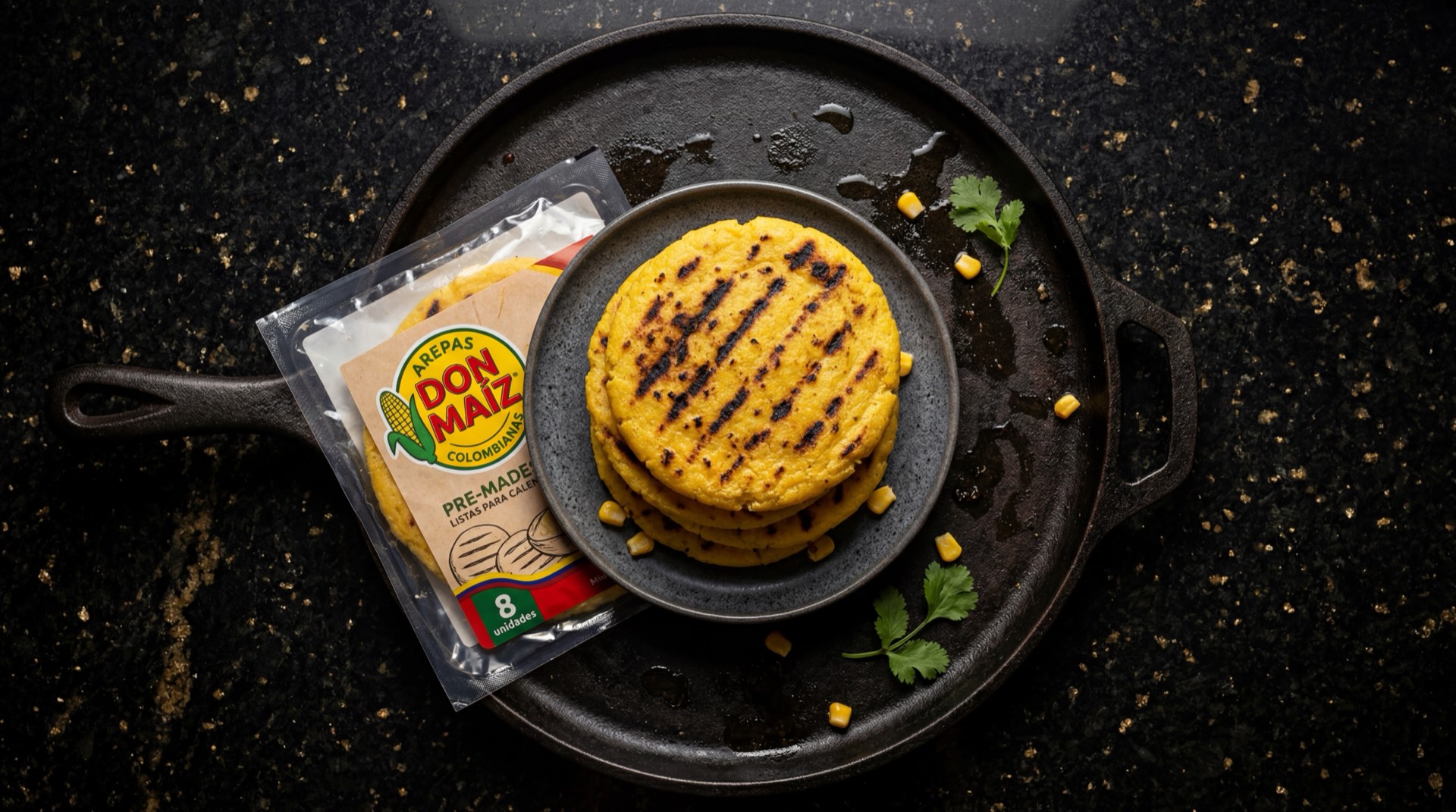 Arepa Don Maiz blanca precocida asada dorada sobre plancha de hierro fundido, fondo de marmol oscuro