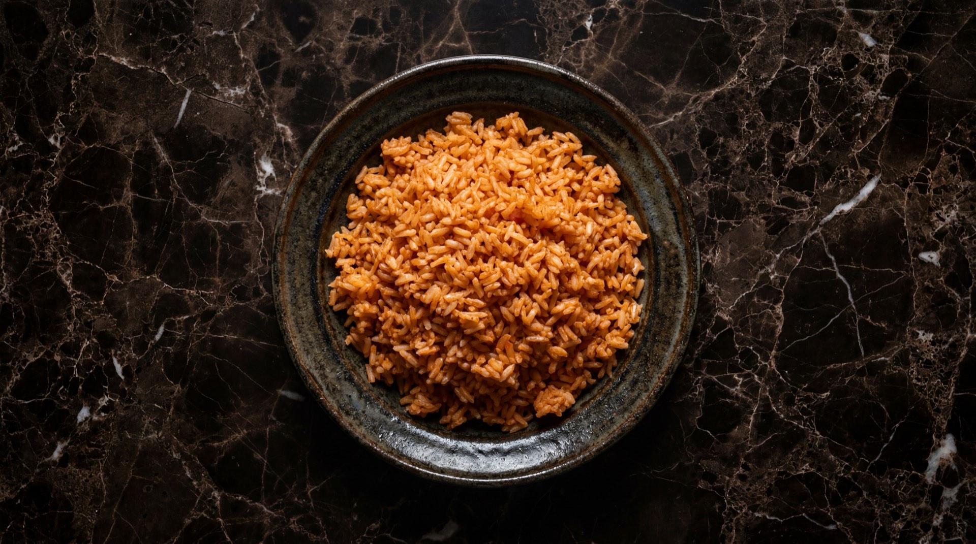 Arroz rojo mexicano con chicharos verdes y zanahoria en plato de ceramica sobre mesa oscura