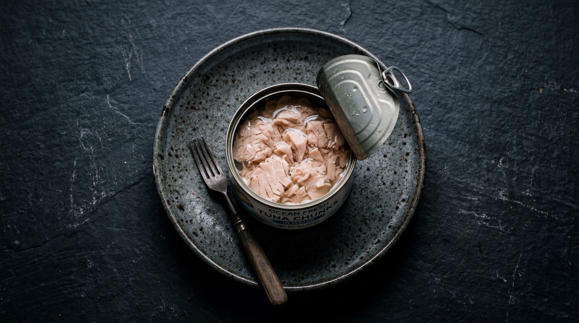Atun enlatado colombiano escurrido desmenuzado sobre plato de ceramica negro mate en mesa de marmol negro con vetas doradas
