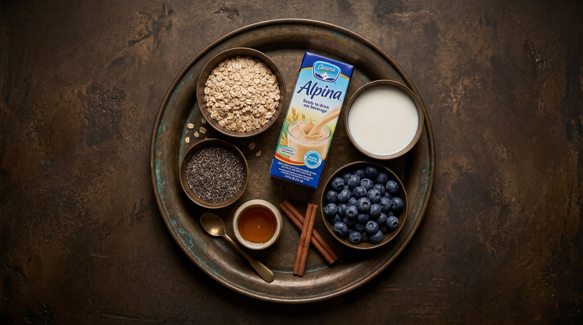 Ingredientes de la Avena Alpina: avena en hojuelas, leche entera liquida, canela en rama, azucar refinada y aceite vegetal sobre mesa oscura