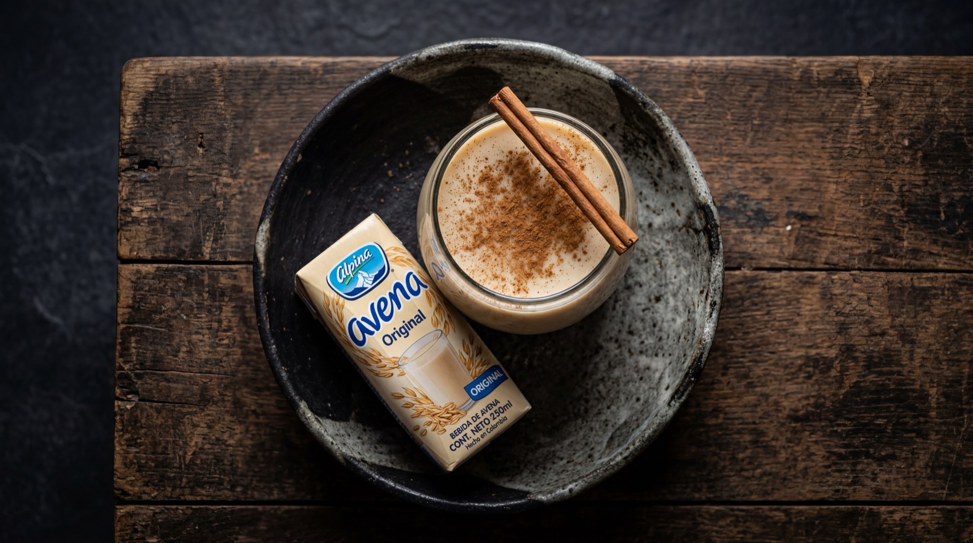 Avena Alpina de Alpina Productos Alimenticios, vaso de bebida de avena con canela sobre mesa de marmol oscuro