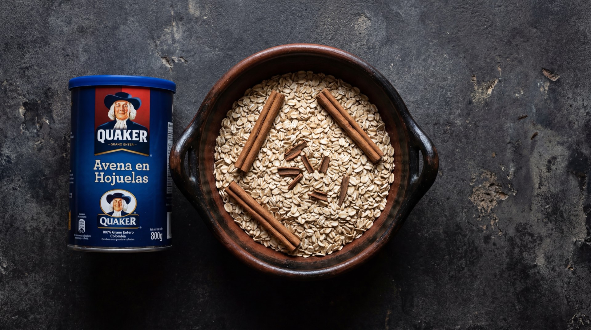 Avena Quaker en hojuelas servida en un bowl con canela en astilla y leche entera sobre mesa de marmol oscuro