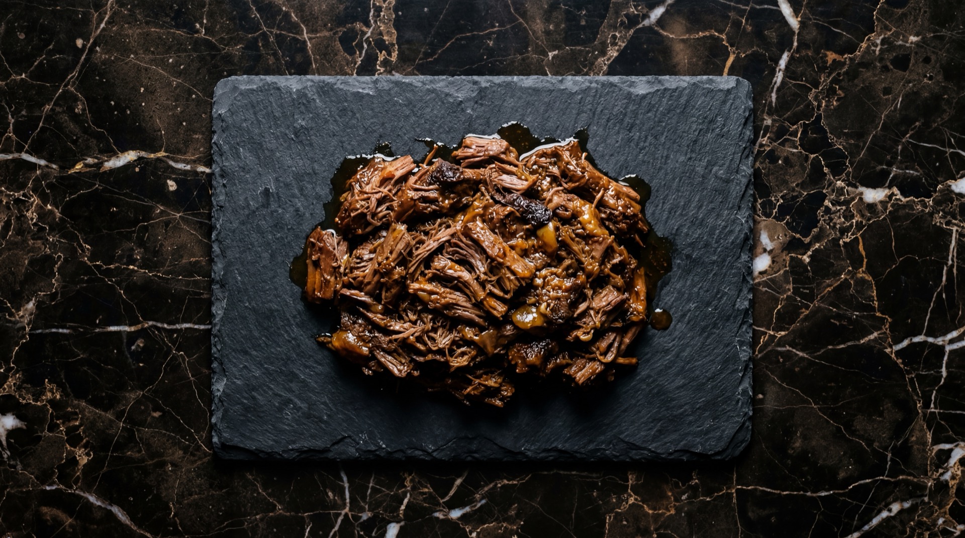 Barbacoa de borrego deshebrada sobre pencas de maguey con cilantro fresco y cebolla blanca picada en plato de barro negro sobre mesa de nogal oscuro