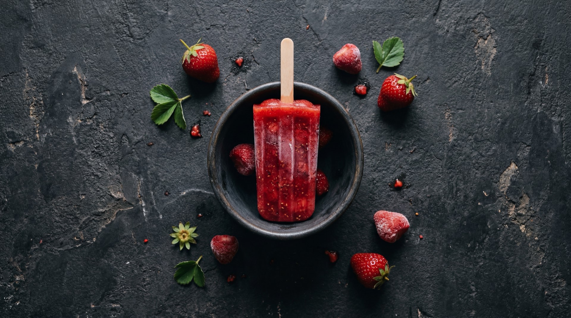 Alternativa saludable al Bon Bon Bum: frutas frescas deshidratadas naturalmente sin azucar con mango, fresa y banano sobre plato de ceramica oscuro