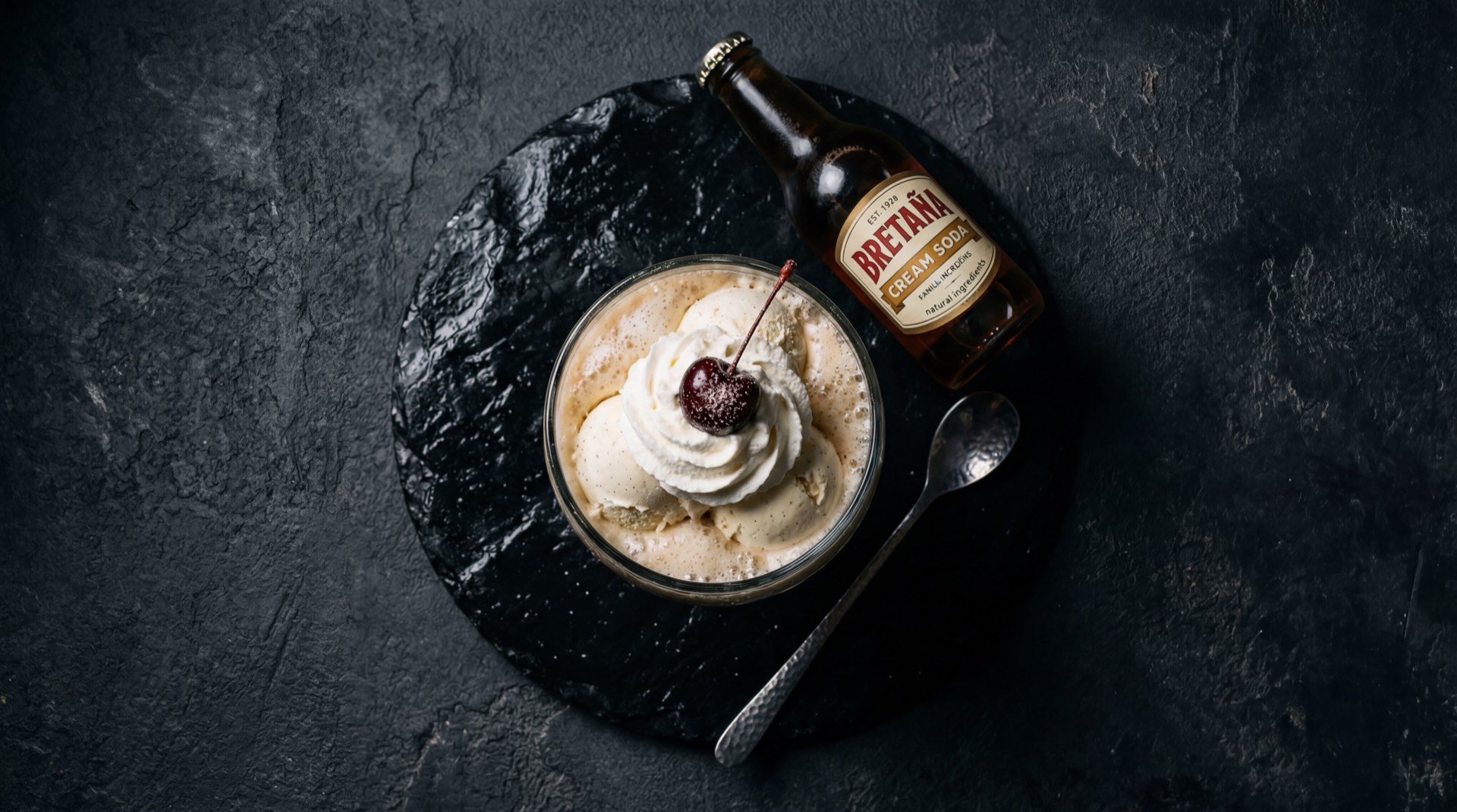 Ingredientes de la Bretana Postobon: agua carbonatada, azucar refinada blanca, saborizante de vainilla natural y colorante rosado, sobre mesa de piedra oscura