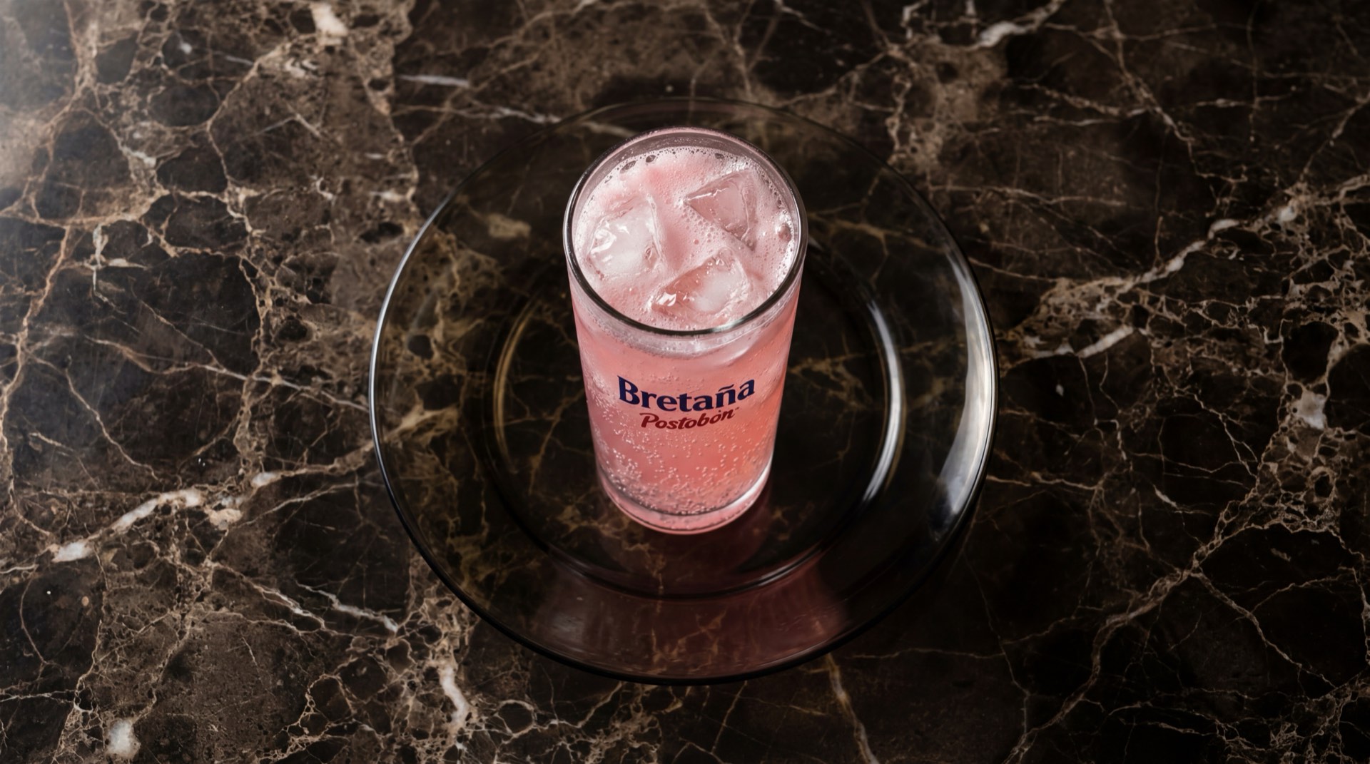 Botella de Bretana de Postobon, gaseosa de crema colombiana color rosado claro sobre mesa de marmol oscuro