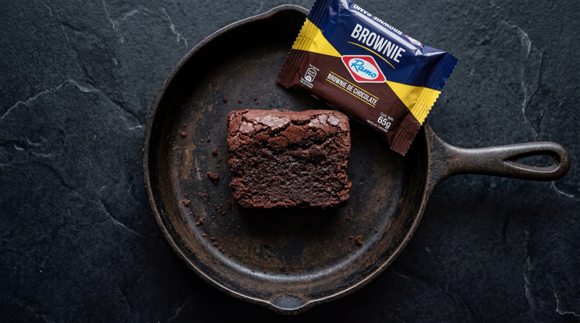 Brownie Ramo individual de chocolate oscuro denso y humedo sobre plato de ceramica negra, mesa de marmol oscuro