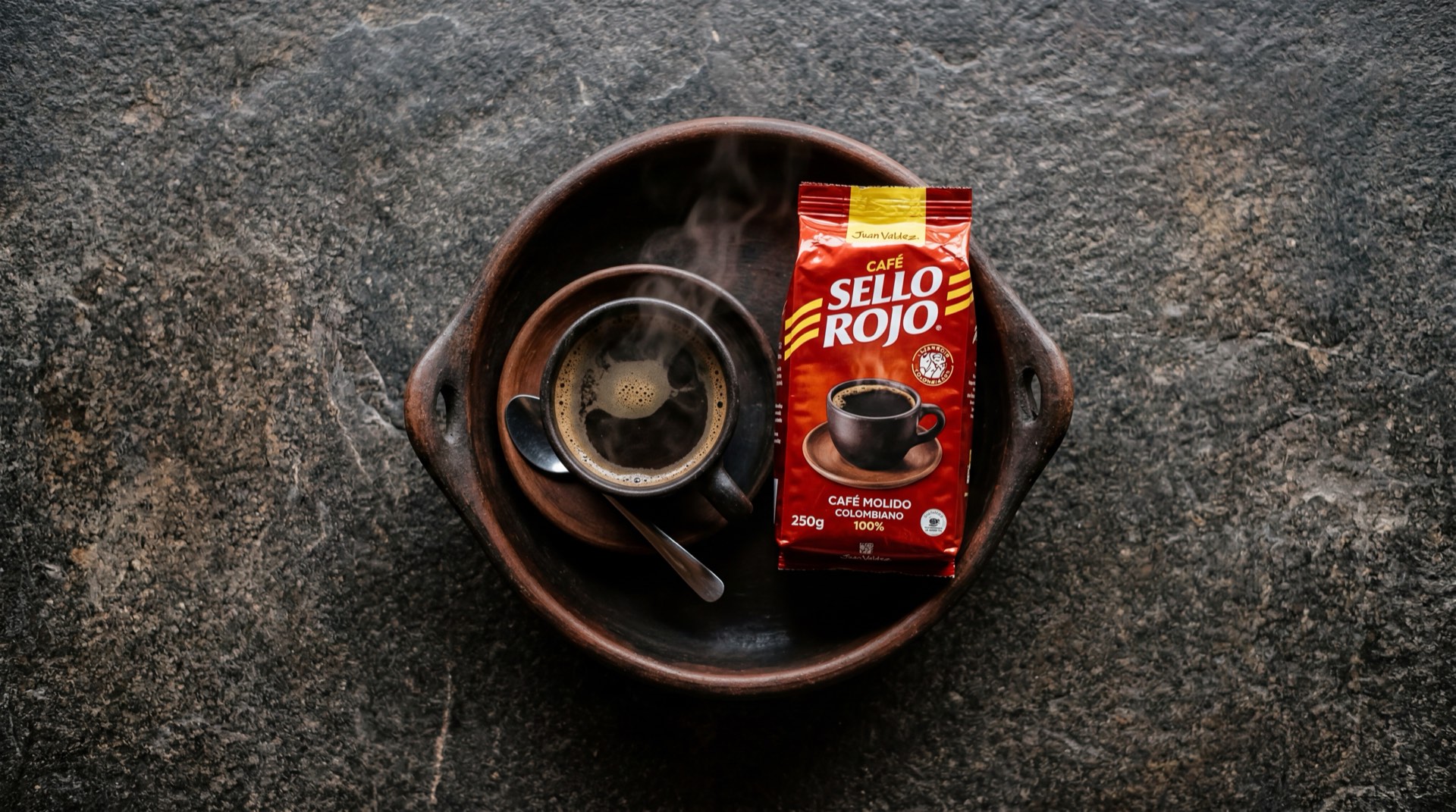 Taza de cafe tinto colombiano preparado con Sello Rojo sobre mesa de marmol oscuro, empaque rojo iconico de Colcafe al lado
