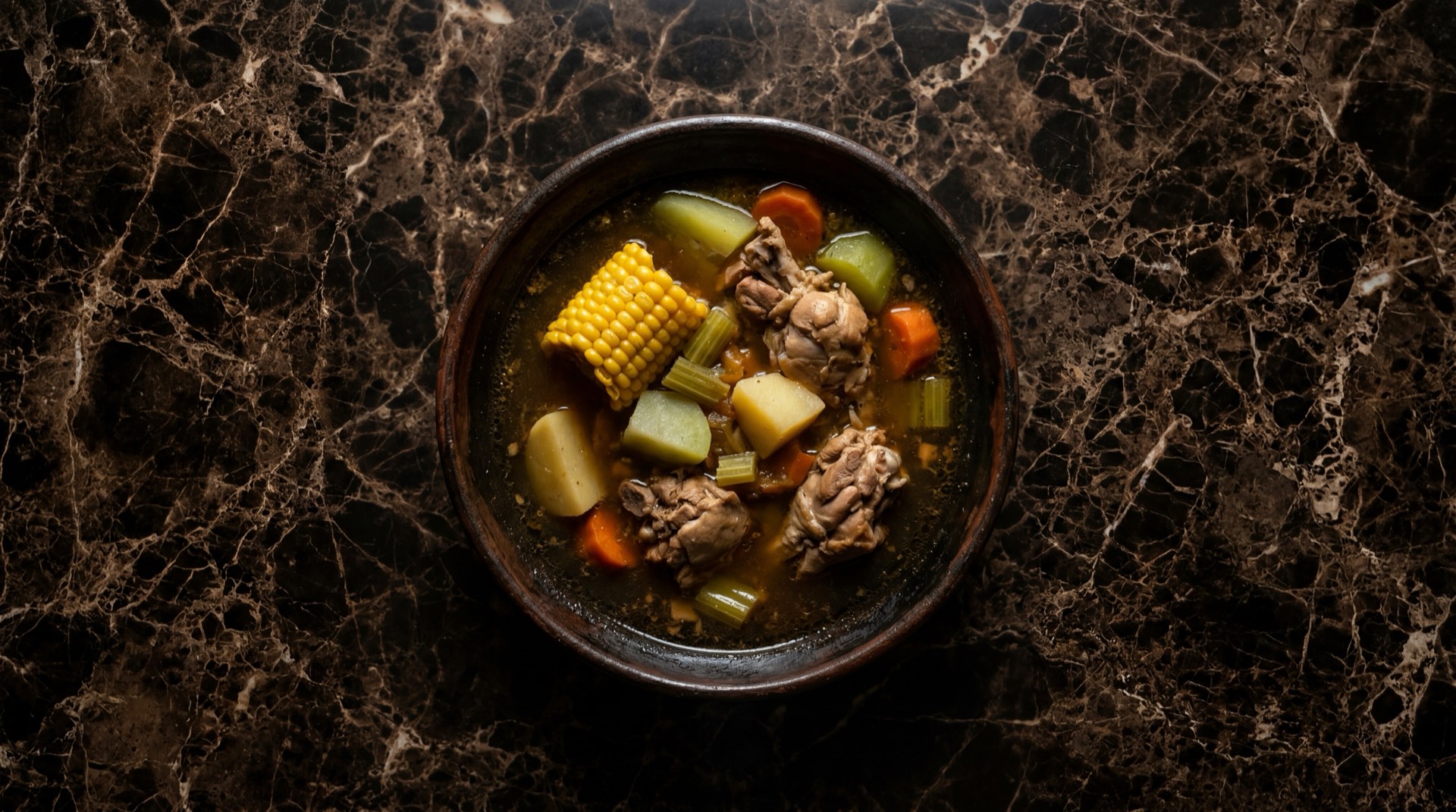 Caldo de pollo mexicano con chayote, elote, calabaza y cilantro fresco en cazuela de barro oscura sobre mesa de piedra caliza negra