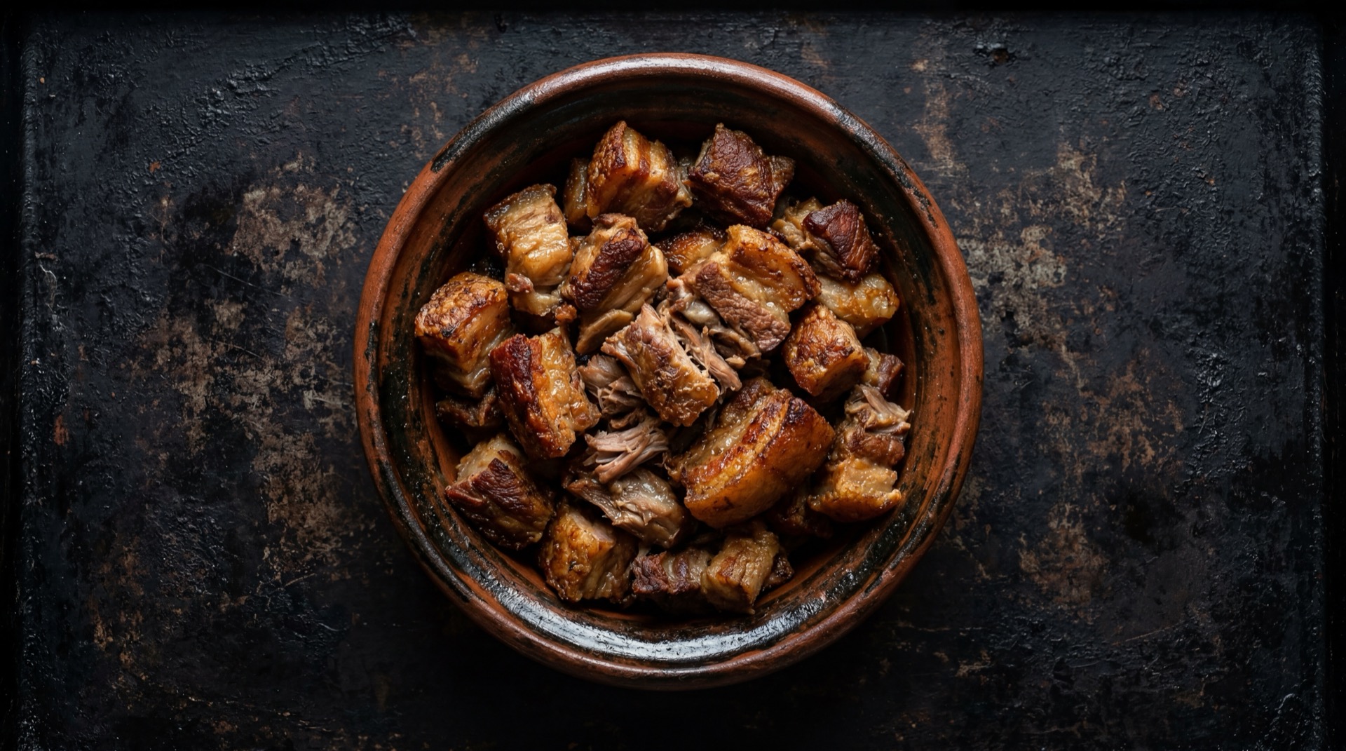 Carnitas michoacanas doradas y crujientes con trozos de carne de cerdo cocida en manteca sobre tabla de madera de acacia oscura sobre mesa de marmol emperador oscuro