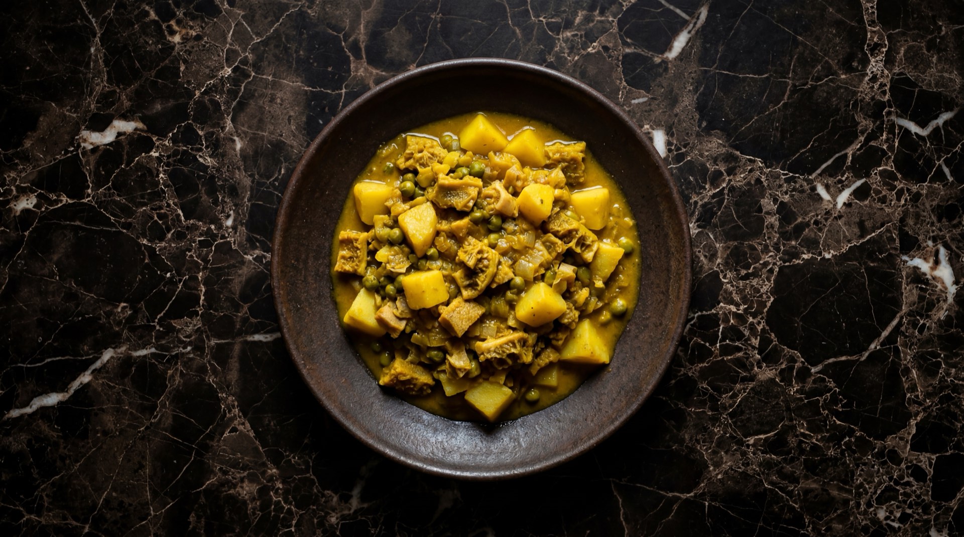 Cau cau peruano de mondongo con papas amarillas y hierbabuena fresca en cuenco de cobre martillado sobre mesa de piedra volcanica oscura