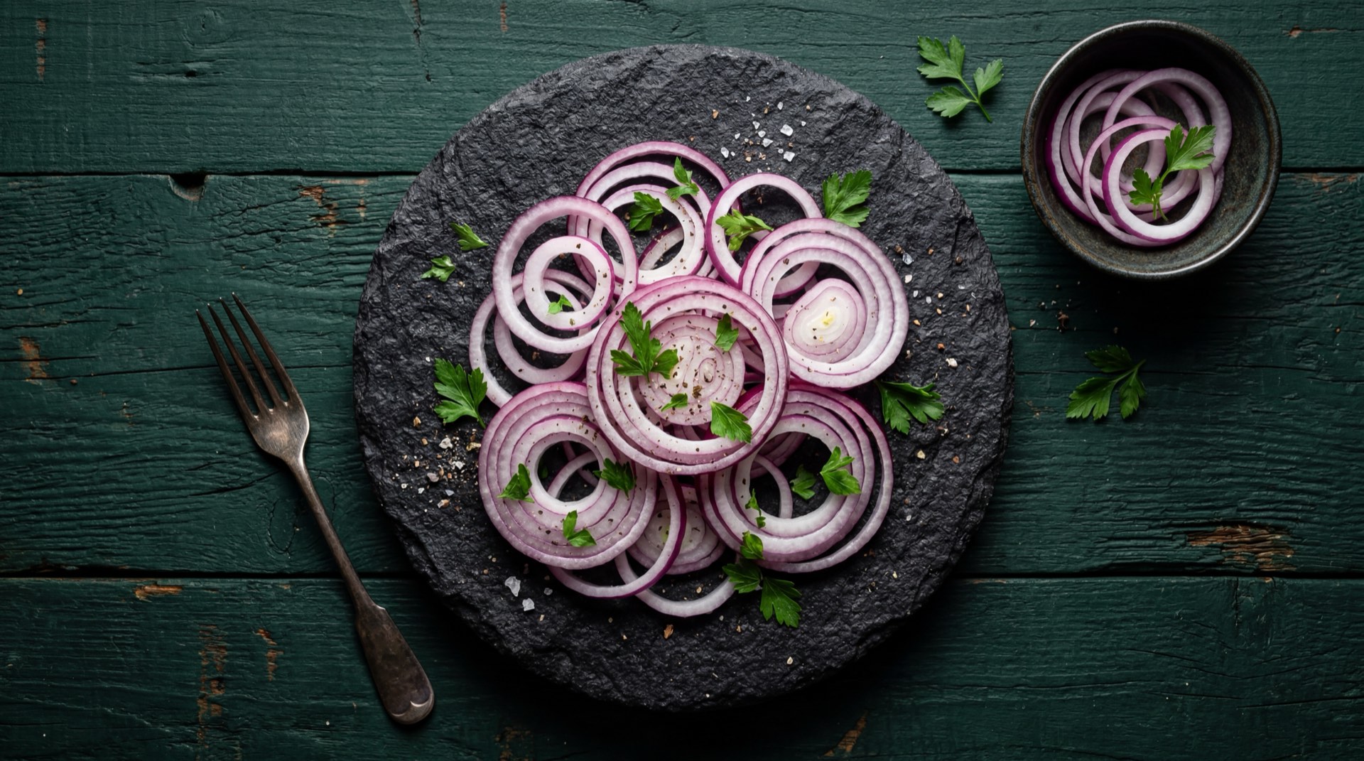 Ensalada fresca de cebolla morada en rodajas con tomate cherry y cilantro fresco sobre plato de piedra volcanica negra