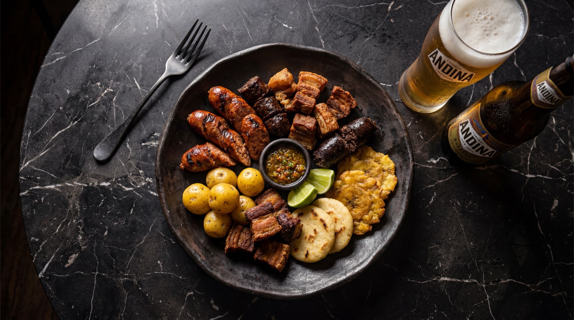 Cerveza Andina colombiana fria en vaso de vidrio con espuma sobre mesa de marmol oscuro