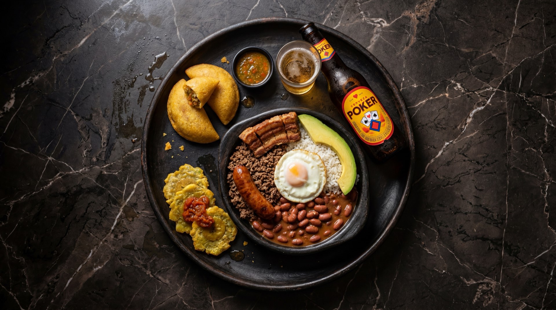 Lata amarilla de cerveza Poker colombiana con vaso de vidrio lleno de cerveza dorada y espuma blanca sobre mesa de terrazzo negro con chips blancos