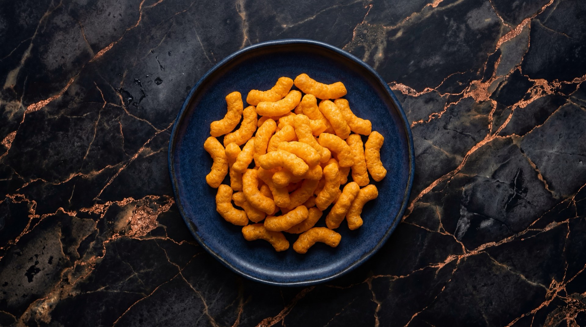 Cheetos originales de Frito Lay Colombia, snacks de maiz inflado con sabor a queso sobre plato de basalto volcanico oscuro