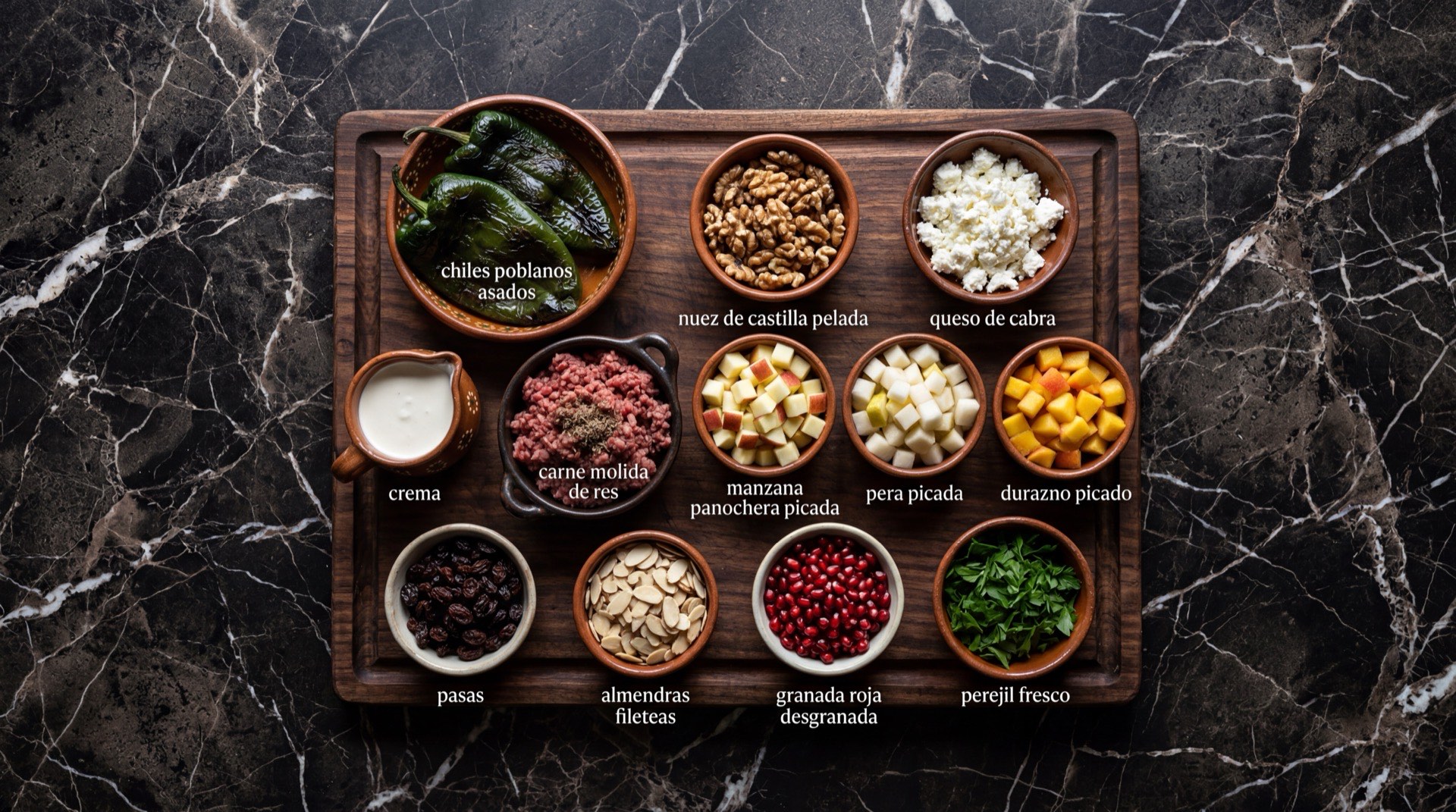 Ingredientes de los chiles en nogada: chiles poblanos frescos asados, carne molida de res y cerdo, duraznos criollos frescos, peras de leche, manzanas panocheras, nuez de Castilla fresca pelada, queso de cabra fresco, granada roja desgranada, perejil fresco y pasas rubias