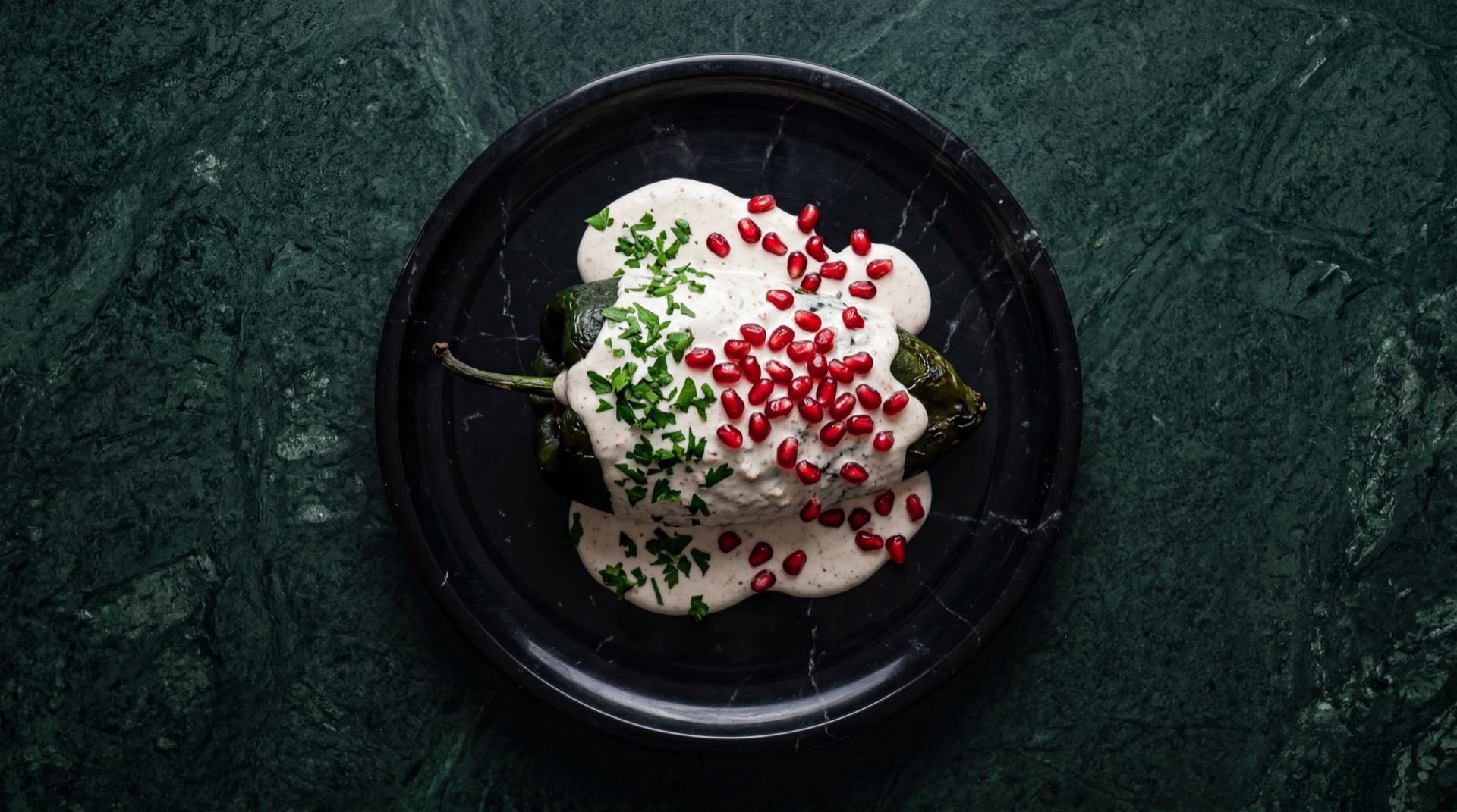 Chiles en nogada poblanos con salsa de nuez de Castilla blanca, granos de granada roja y hojas de perejil fresco en plato de talavera azul