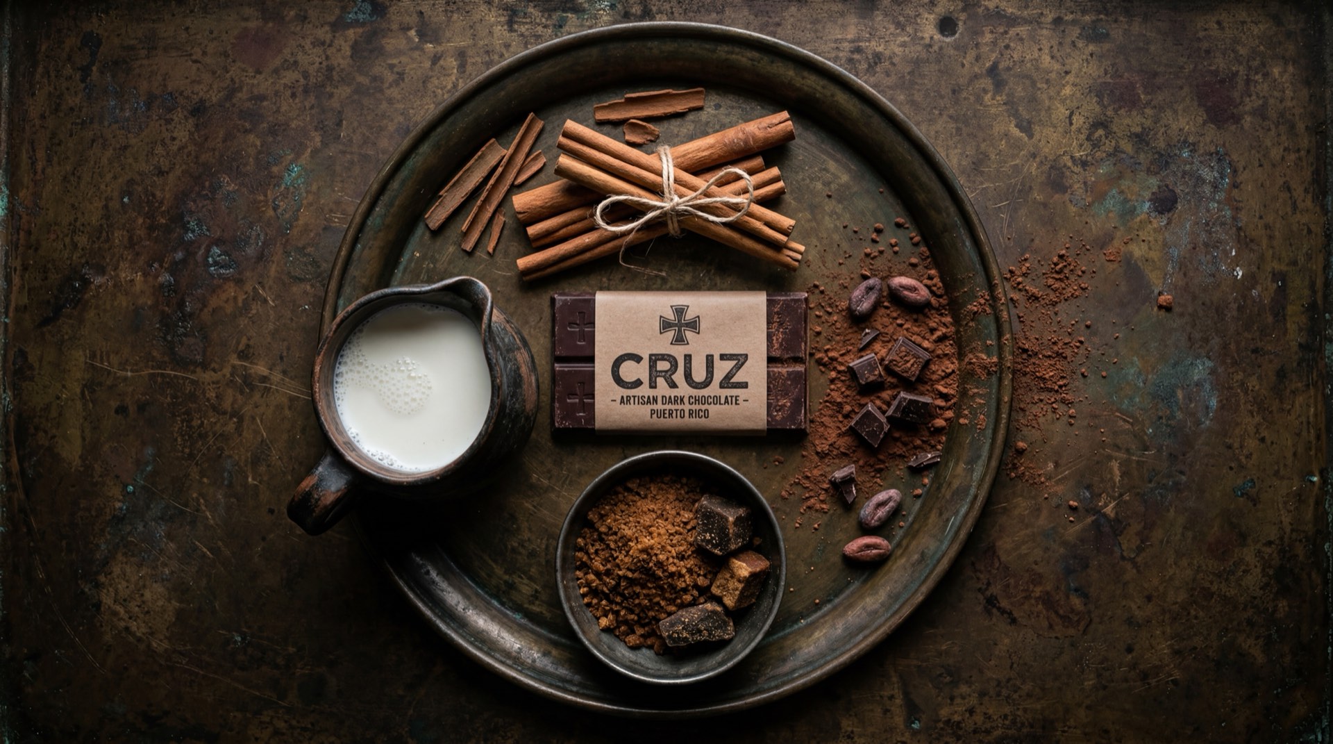 Pastillas de Chocolate Cruz abiertas mostrando la textura del chocolate de mesa, junto a cacao en polvo, azucar granulada y canela en rama sobre superficie oscura