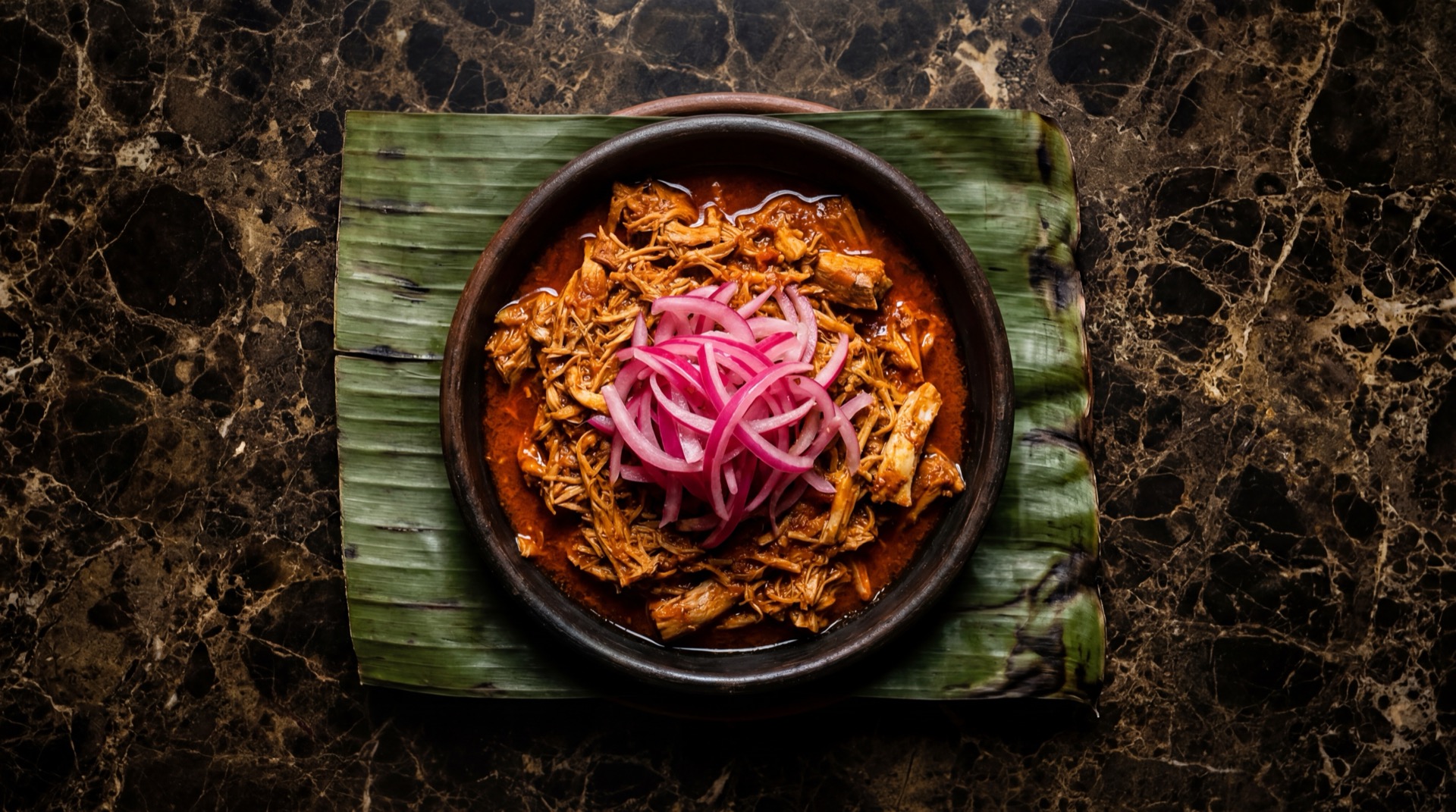 Cochinita pibil yucateca deshebrada con cebolla morada curtida en plato de barro sobre mesa de madera oscura