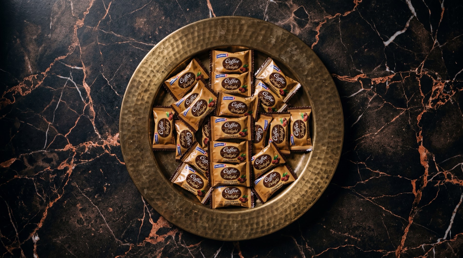 Caramelos Coffee Delight de Colombina envueltos individualmente sobre plato de ceramica negra en mesa de marmol oscuro