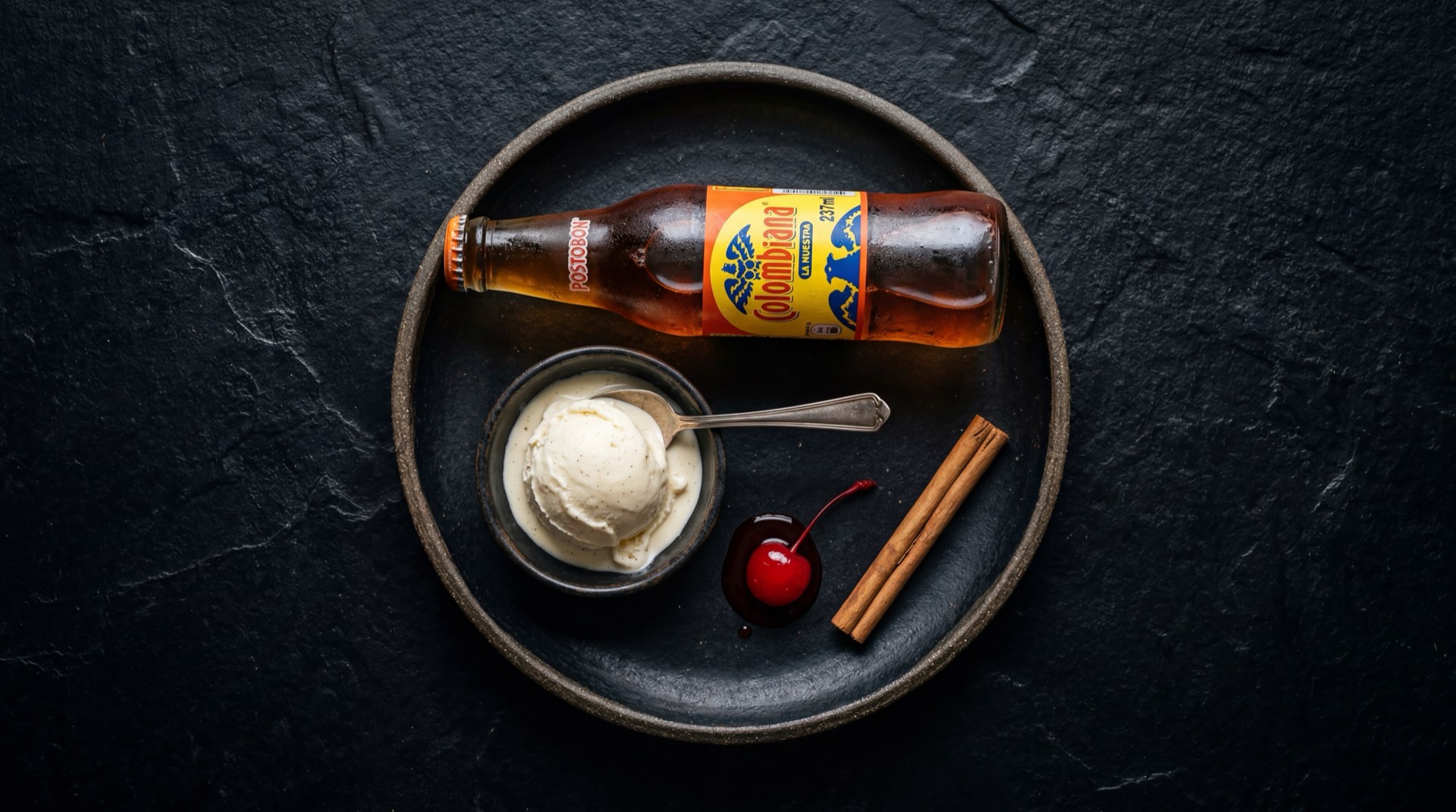 Colombiana Postobon servida en vaso de vidrio con hielo mostrando el liquido dorado ambar gasificado, con azucar refinada blanca y limones verdes frescos al lado
