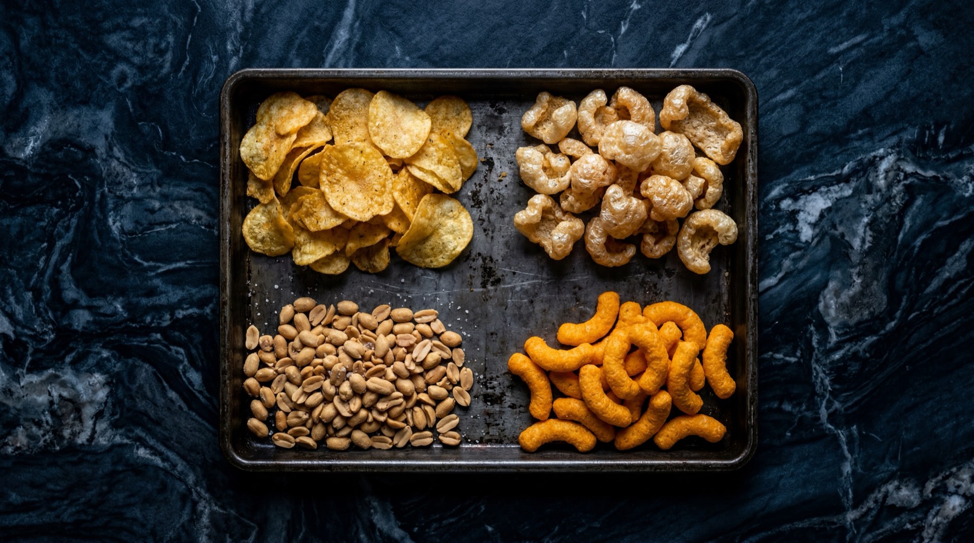 Componentes del De Todito: papas fritas Margarita natural, Cheetos boliqueso de maiz, chicharron crujiente de harina de trigo y mani salado tostado separados sobre superficie oscura