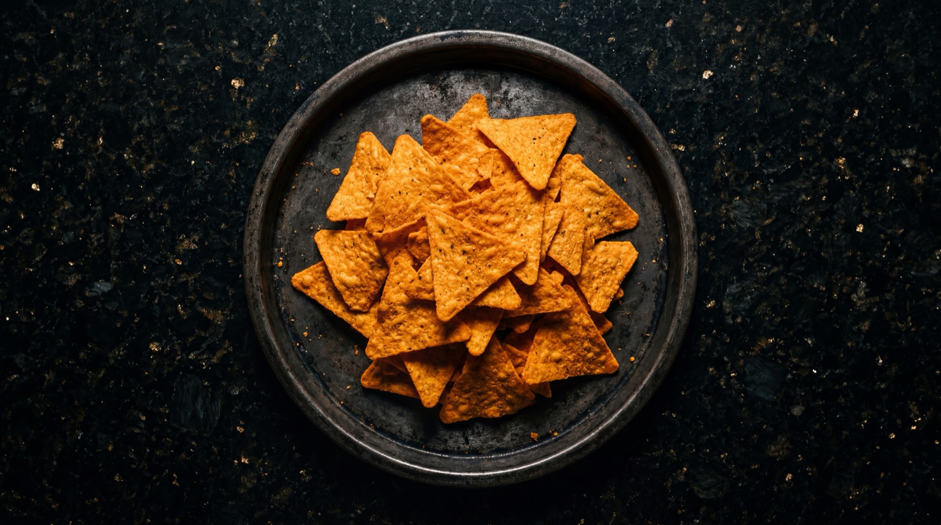 Doritos Queso Nacho de Frito Lay Colombia, tortillas de maiz triangulares con polvo de queso naranja sobre plato de obsidiana negra
