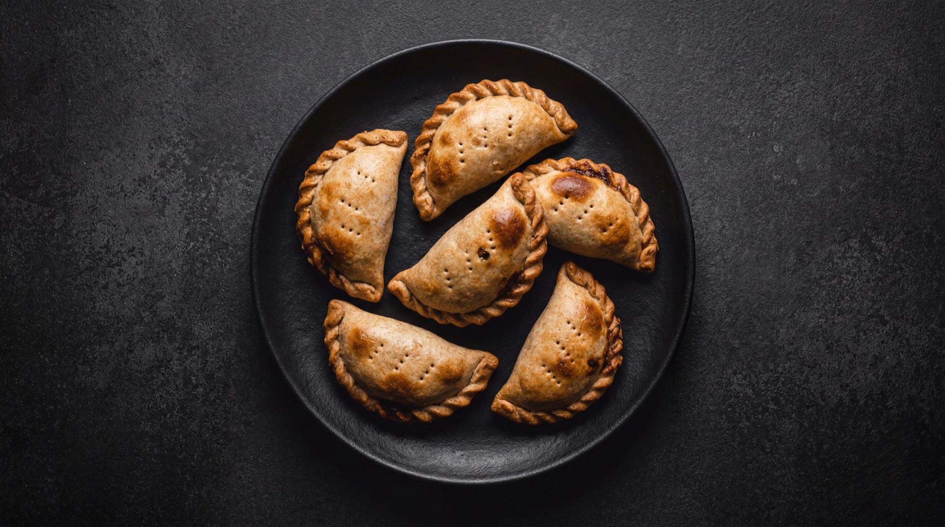 Empanadas argentinas saludables al horno con relleno de pollo y verduras sobre bandeja de ceramica oscura