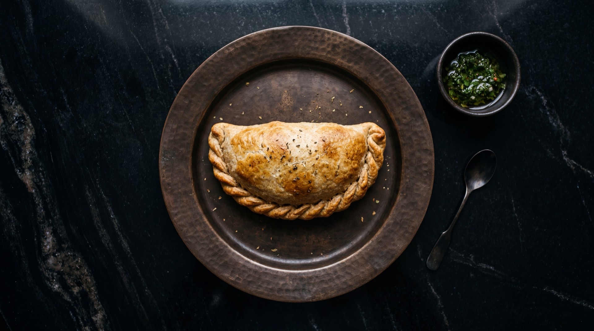 Empanada Dona Chepa al horno dorada con ensalada fresca de tomate rojo maduro, aguacate Hass y cebolla morada sobre plato oscuro