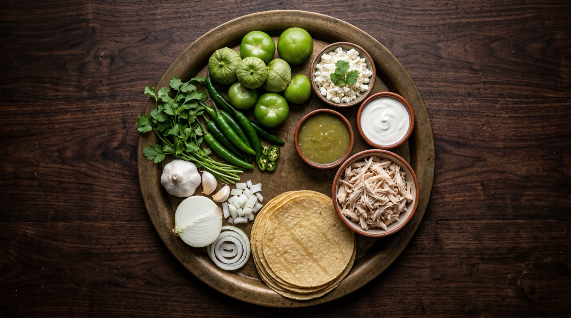 Ingredientes para enchiladas verdes mexicanas: tomatillos verdes frescos sin cascara, chiles serranos frescos, pechuga de pollo deshebrada, tortillas de maiz frescas, crema agria mexicana, queso fresco, cilantro fresco con tallos, cebolla blanca y ajo fresco