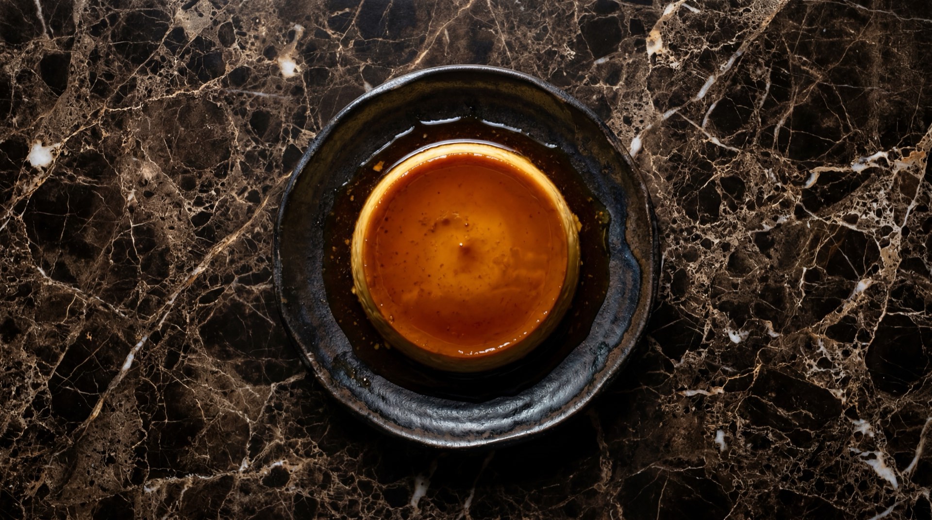 Flan mexicano napolitano con caramelo dorado en plato de ceramica negra sobre mesa de granito negro con vetas doradas