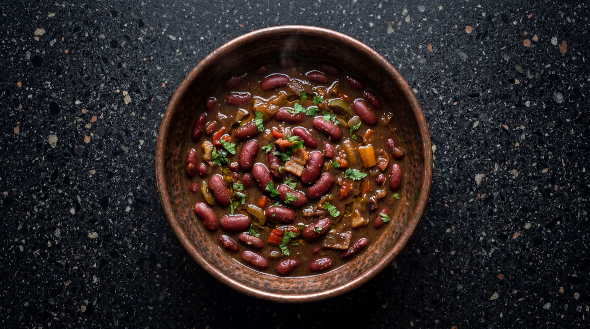 Frijoles colombianos antioquenos con caldo espeso cremoso servidos en cazuela de barro sobre mesa de marmol negro