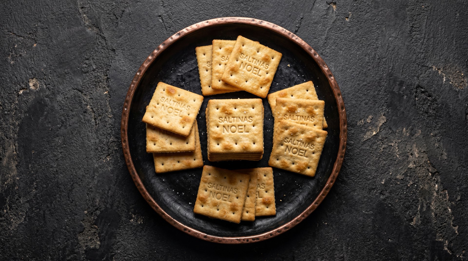 Galletas Saltinas de Noel en paquete abierto sobre mesa de marmol oscuro, galletas de soda cracker doradas y crujientes