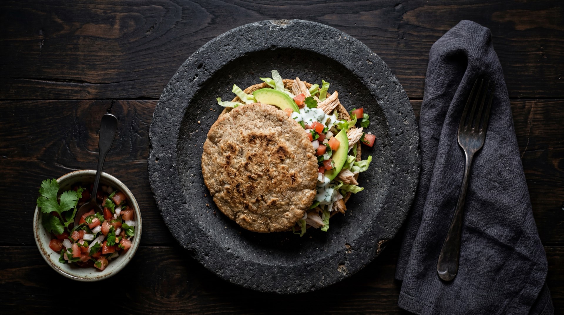 Gorditas mexicanas version saludable al comal sin freir, rellenas de frijoles negros refritos, pollo desmenuzado, lechuga iceberg y poca crema agria sobre plato de ceramica oscuro