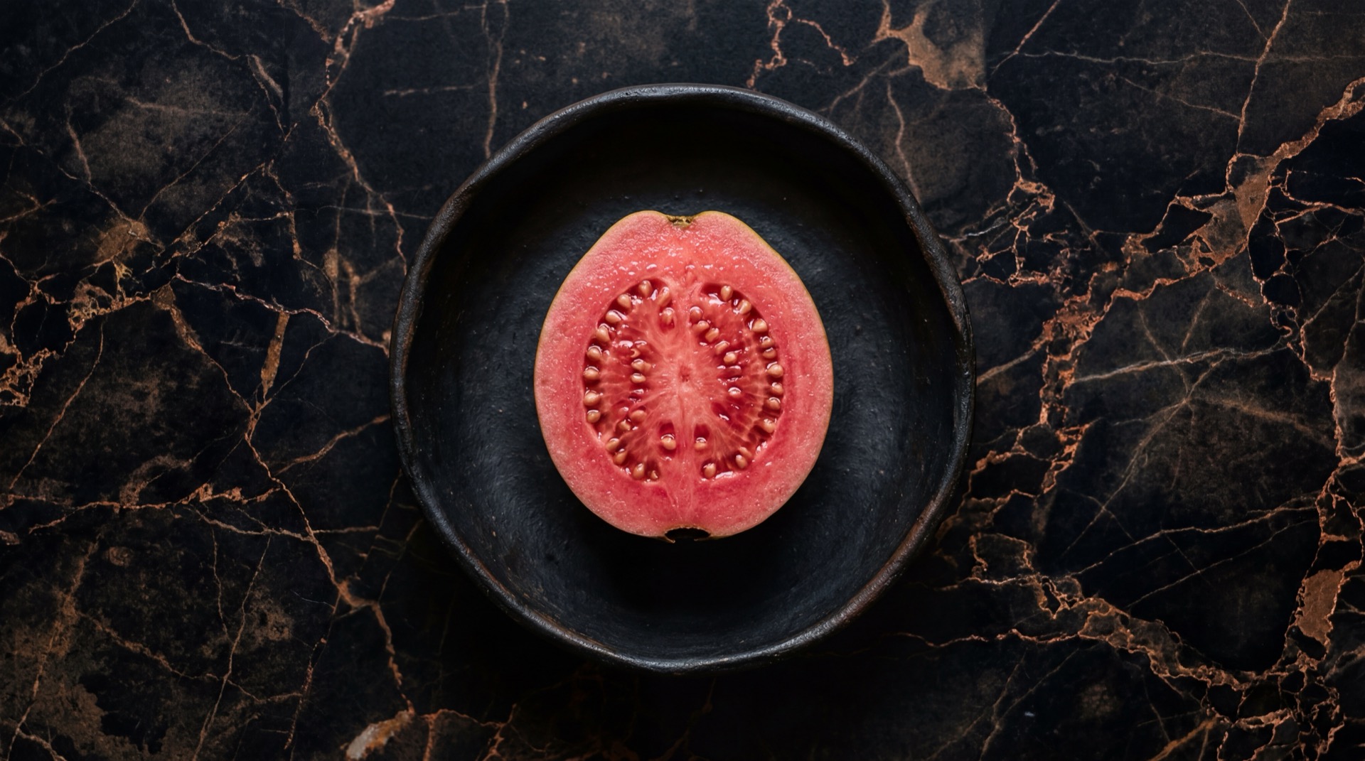 Guayaba rosada colombiana madura cortada por la mitad mostrando pulpa rosada con semillas sobre plato de ceramica negra