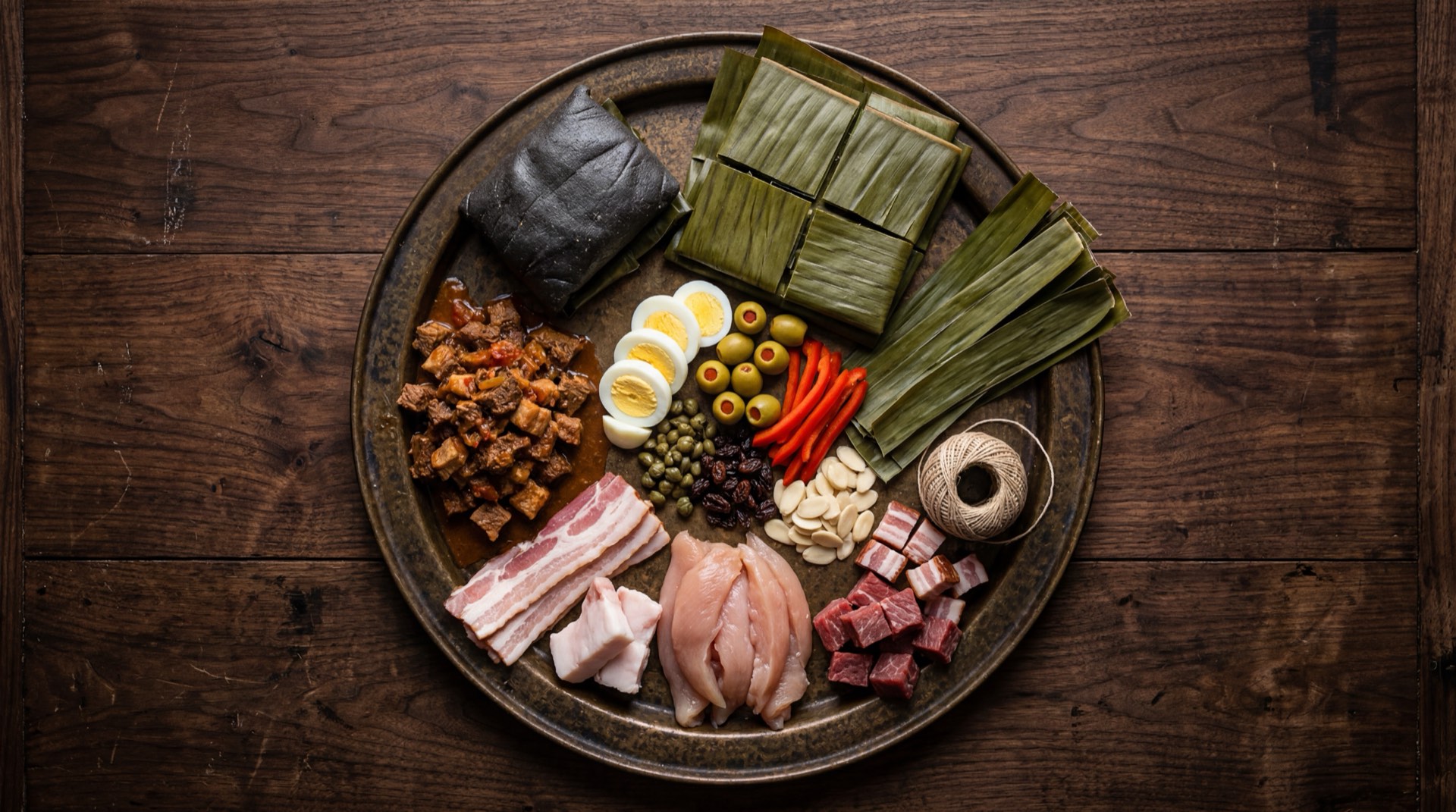 Ingredientes de la hallaca venezolana: harina de maiz precocida blanca, aceite con onoto achiote, falda de res cruda en trozos, pernil de cerdo crudo en trozos, pechuga de pollo entera, aceitunas verdes rellenas de pimenton, alcaparras escurridas, pasas rubias, encurtidos en vinagre, cebolla blanca grande, ajies dulces venezolanos, pimenton rojo, dientes de ajo fresco y hojas de platano frescas