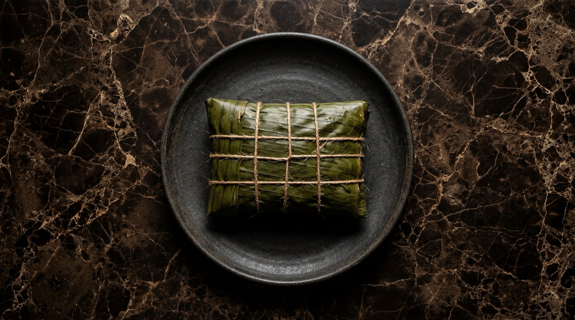 Hallaca venezolana navidena abierta mostrando el guiso de carne de res, cerdo y pollo con aceitunas verdes rellenas, alcaparras y pasas rubias sobre hoja de platano en mesa de piedra caliza oscura