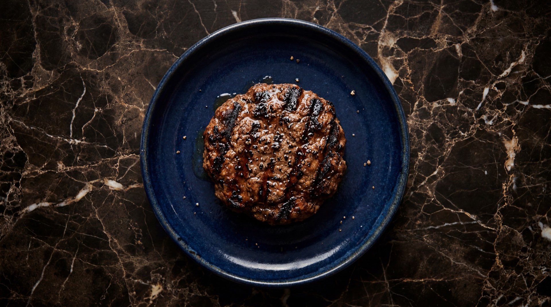 Carne para hamburguesa Zenu asada a la plancha sobre sarten de hierro negro con marcas de grill visibles