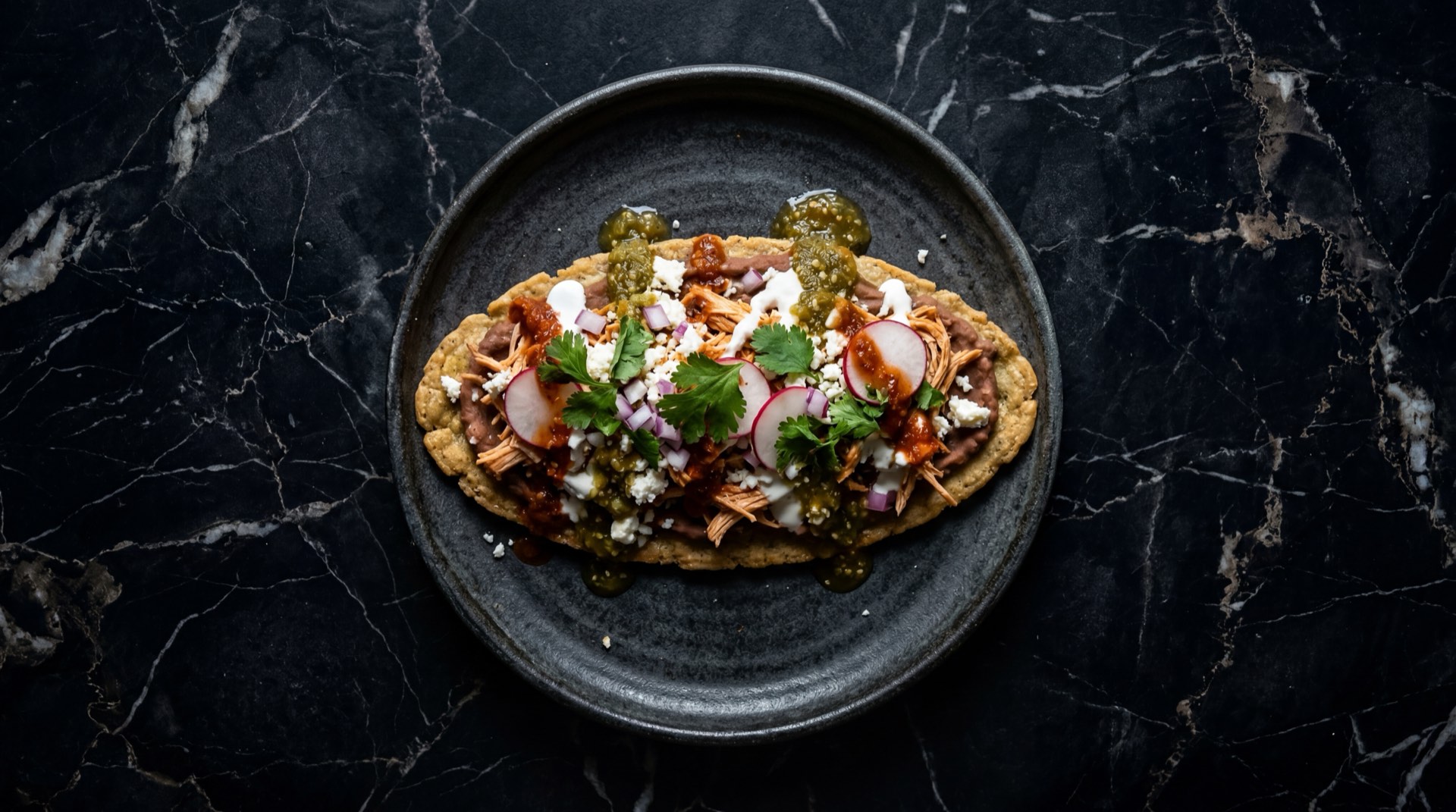 Huaraches mexicanos con frijoles negros refritos, salsa verde de tomatillo, crema agria mexicana y queso fresco desmoronado sobre comal de hierro