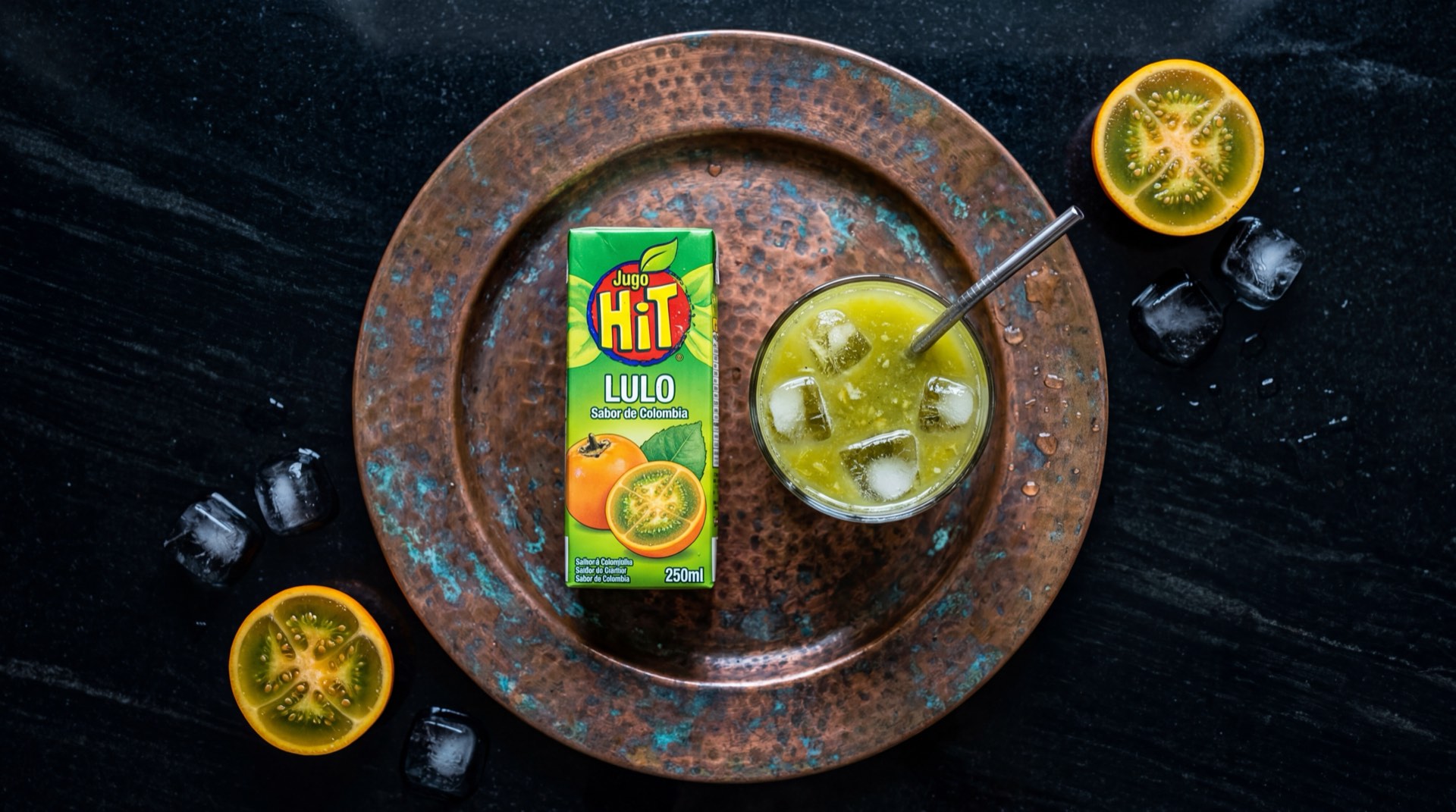 Caja de jugo Hit de lulo de Postobon junto a lulos frescos enteros sobre superficie oscura