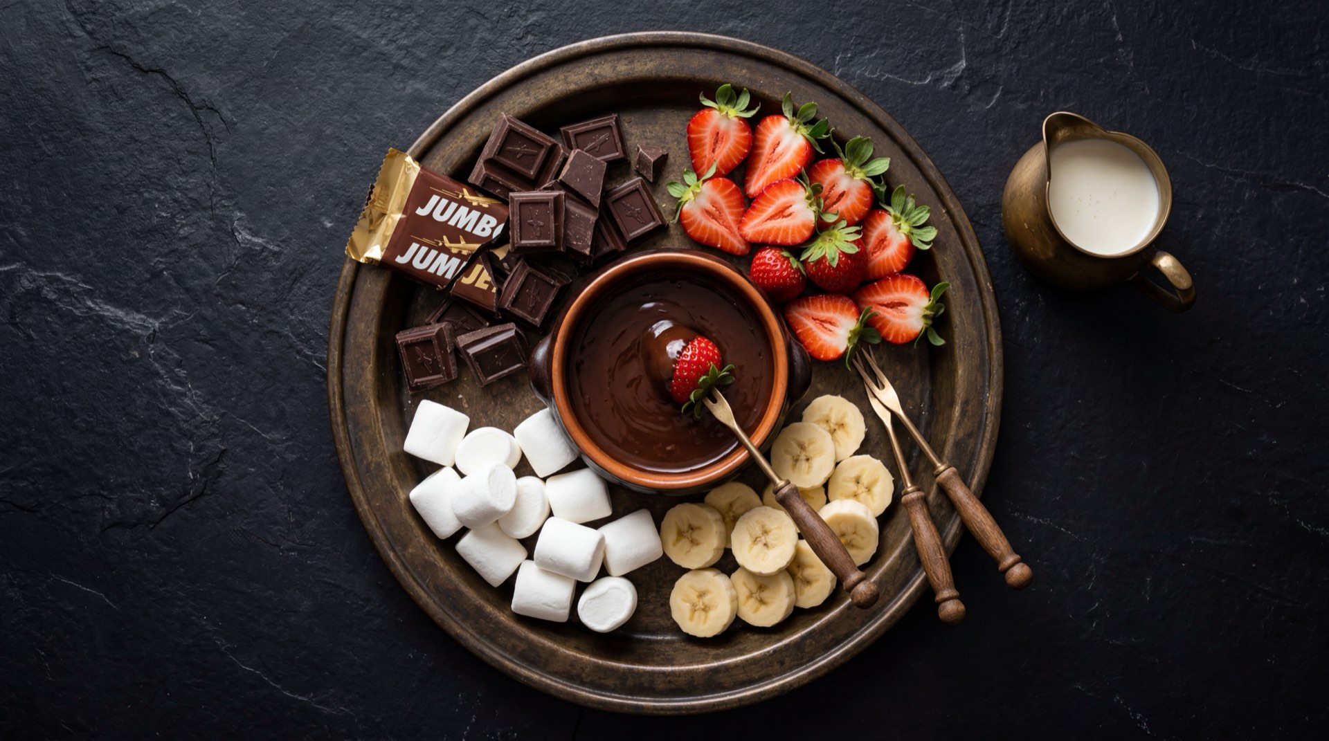 Barra de Jumbo Jet partida mostrando el chocolate con leche solido por dentro, con trozos de cacao tostado, azucar refinada y leche en polvo al lado