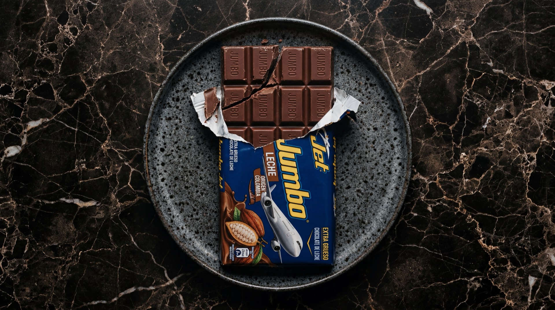Jumbo Jet de Nacional de Chocolates, barra de chocolate con leche gigante sobre plato de ceramica oscura en mesa de marmol negro