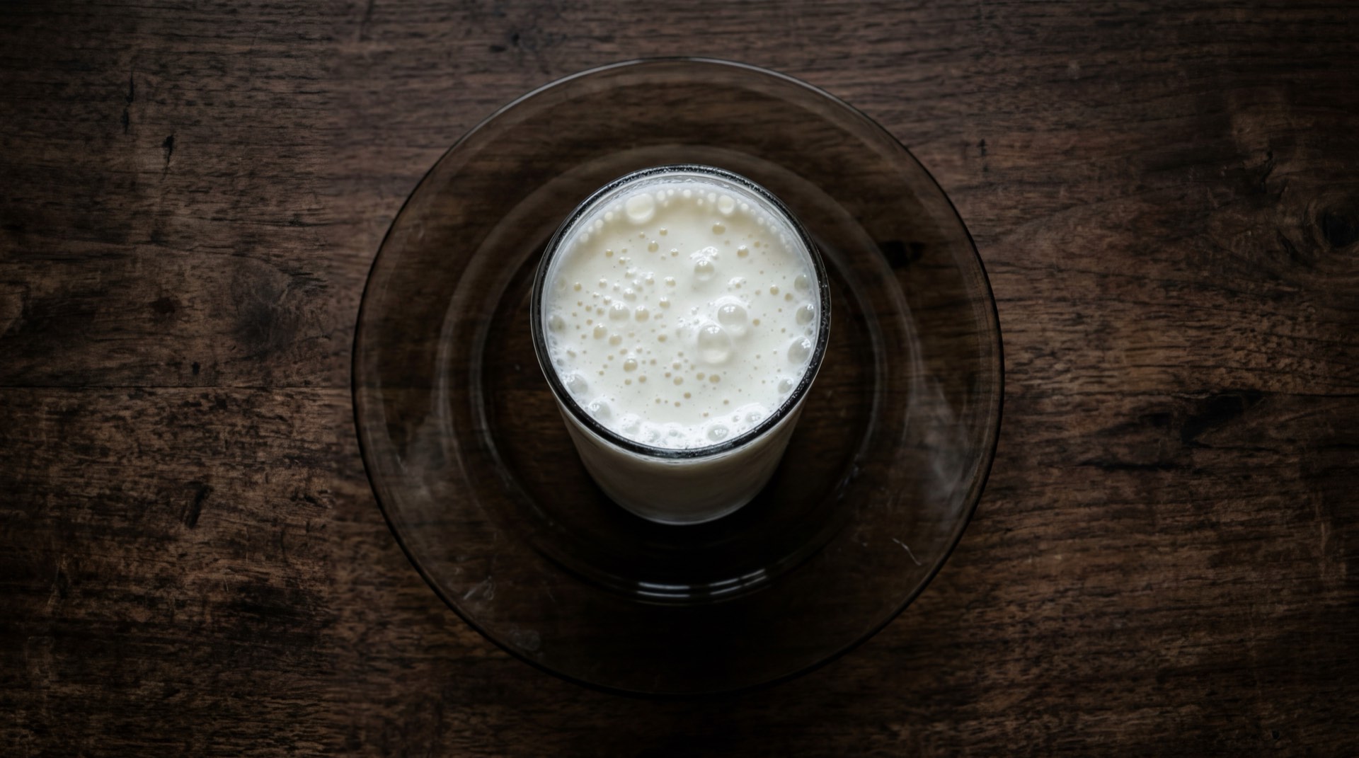 Kumis Alpina en botella de vidrio servido en vaso de cristal sobre mesa de marmol oscuro, bebida fermentada de leche colombiana cremosa y blanca