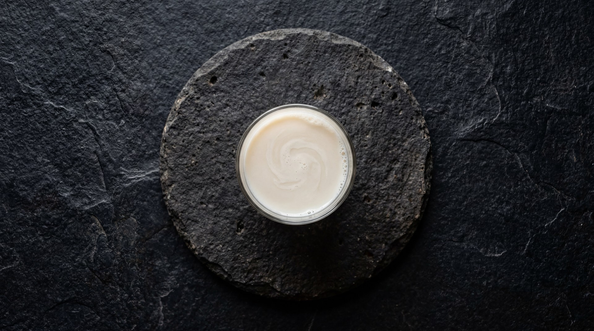 Vaso de leche Alqueria semidescremada con avena en hojuelas y canela en polvo sobre mesa oscura