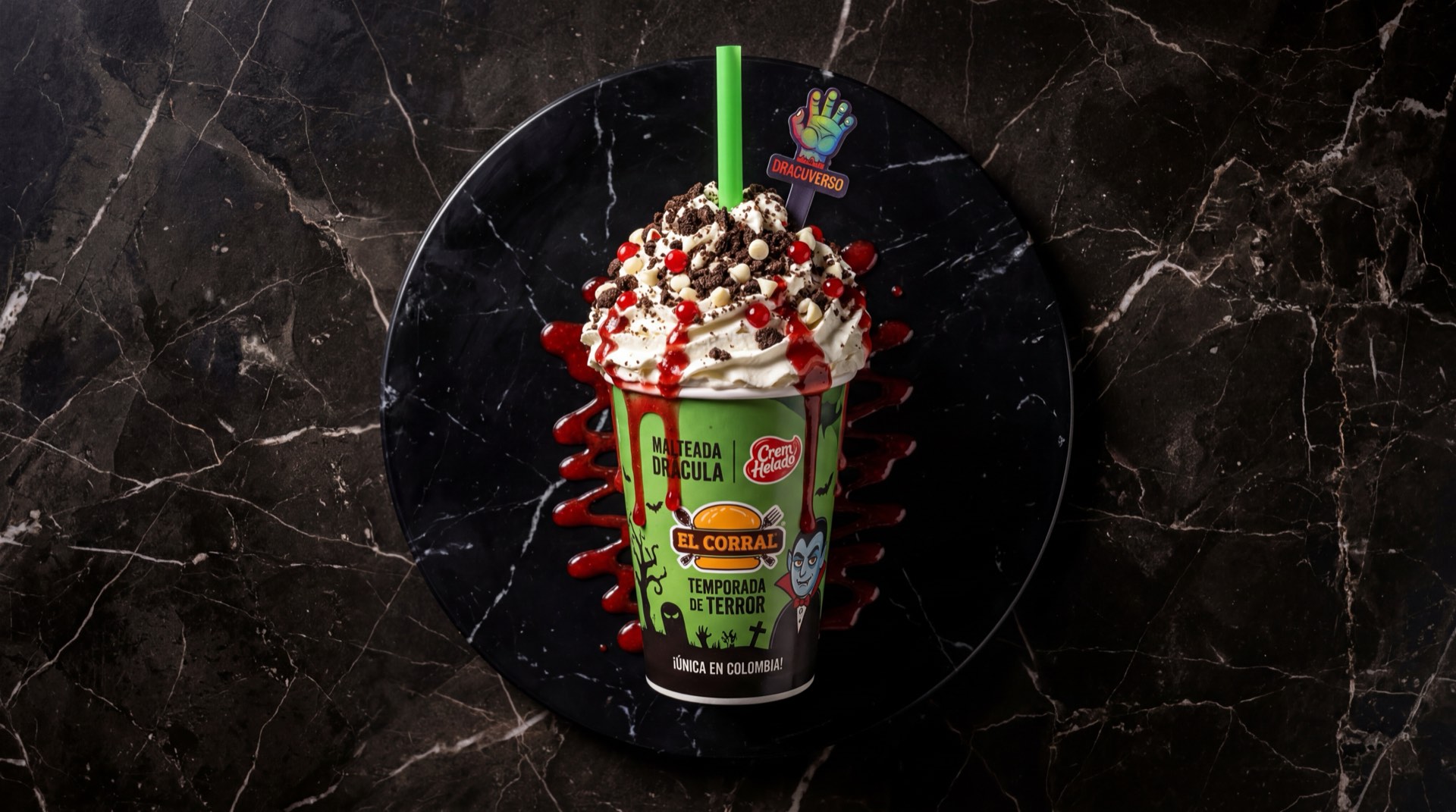 Malteada Dracula de El Corral vista de cerca con crema batida, salsa roja estilo sangre, trozos de galleta y pitillo verde